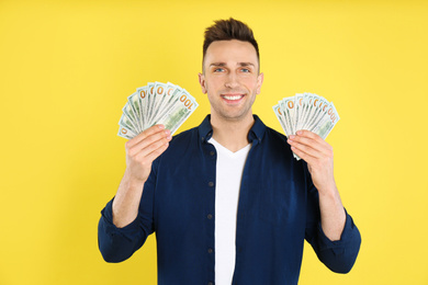 Happy man with cash money on yellow background