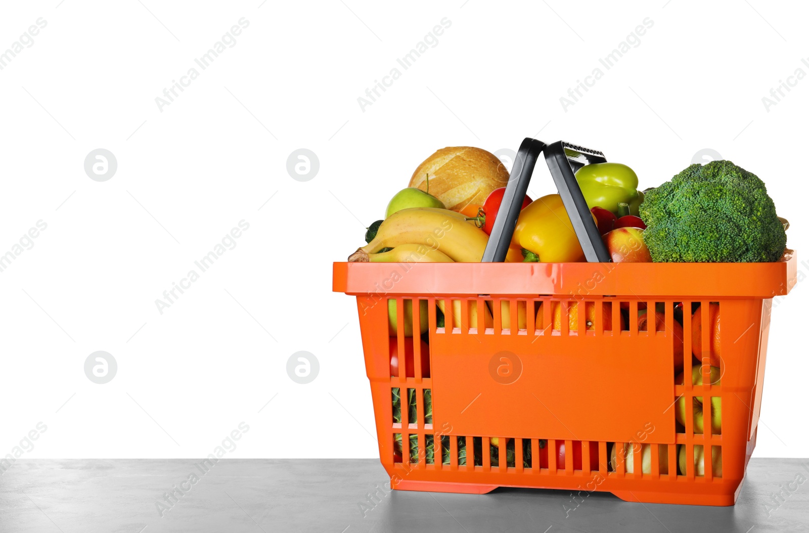 Photo of Shopping basket with grocery products on grey table against white background. Space for text