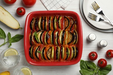 Photo of Delicious ratatouille in baking dish and ingredients on white wooden table, flat lay