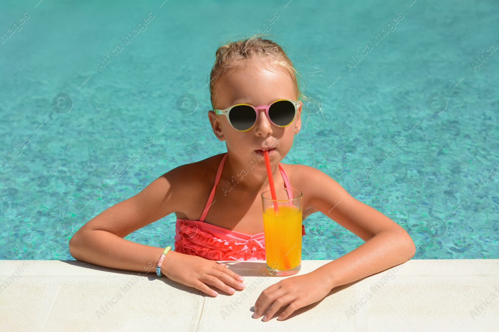 Photo of Cute little girl with glass of juice at swimming pool edge on sunny day