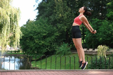 Beautiful woman in sportswear jumping in park. Space for text