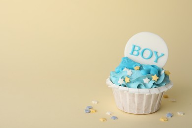 Delicious cupcake with light blue cream and Boy topper on beige background, space for text. Baby shower party