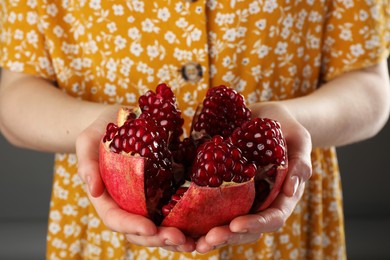 Woman holding fresh pomegranate on dark background, closeup