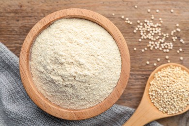 Photo of Quinoa flour in bowl and spoon with seeds on wooden table, flat lay