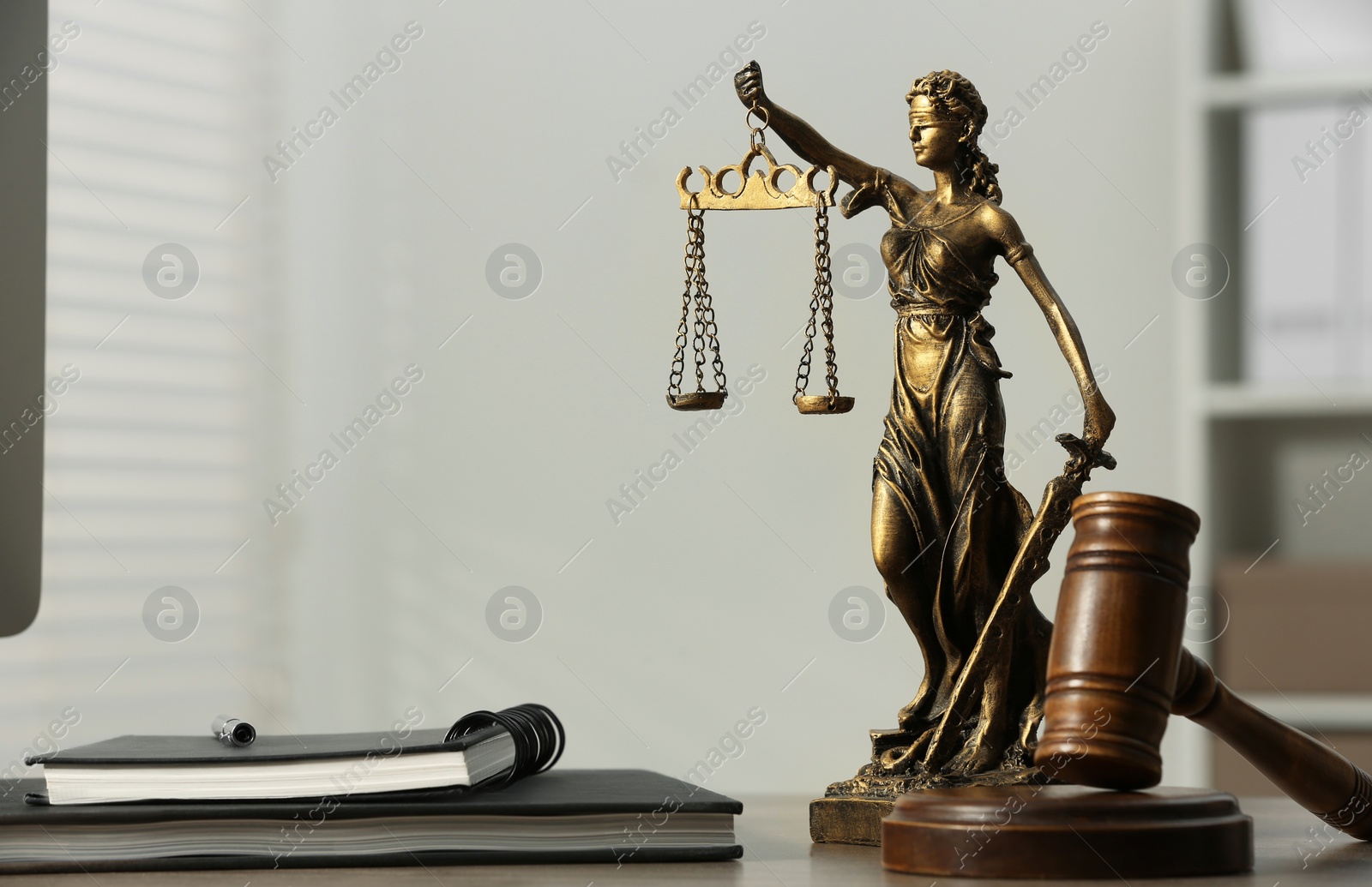 Photo of Figure of Lady Justice, gavel and notebooks on table indoors, space for text. Symbol of fair treatment under law