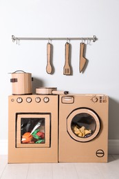 Photo of Cardboard kitchen and washing machine near white wall indoors