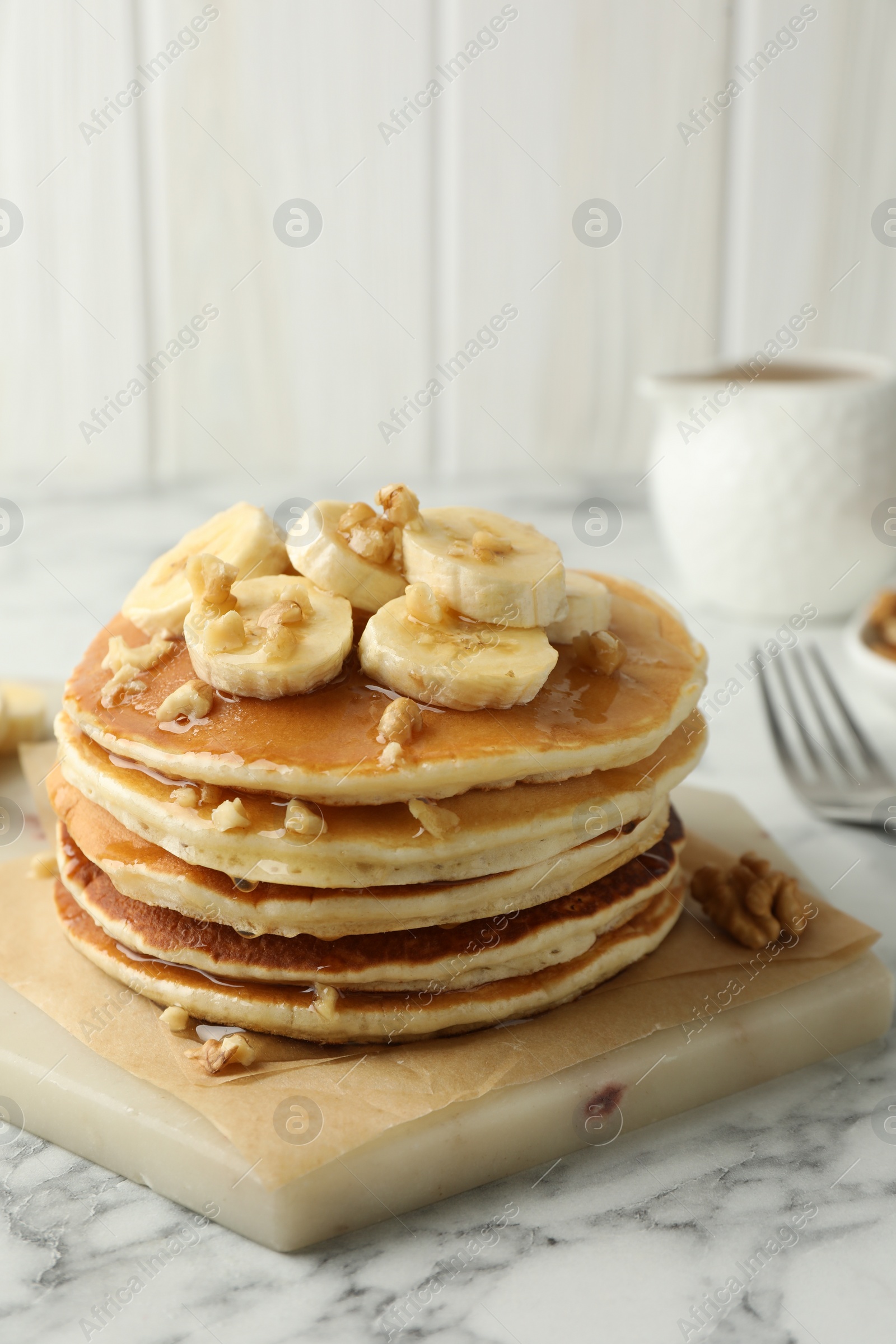 Photo of Delicious pancakes with bananas, walnuts and honey on white marble table