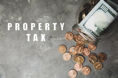 Image of Text Property Tax near jar with dollars and coins on grey table, top view