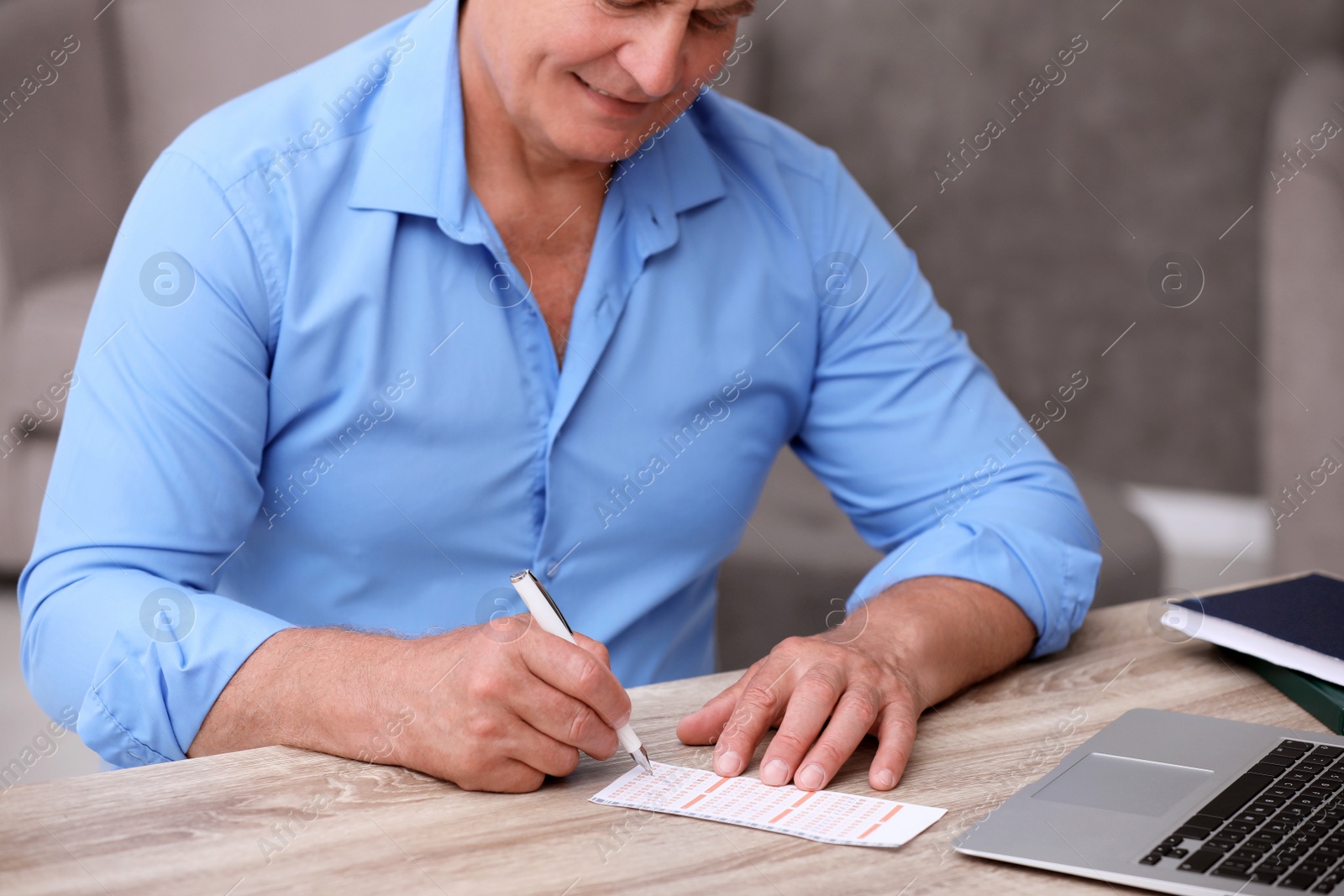 Photo of Senior man filling out lottery ticket at table, closeup