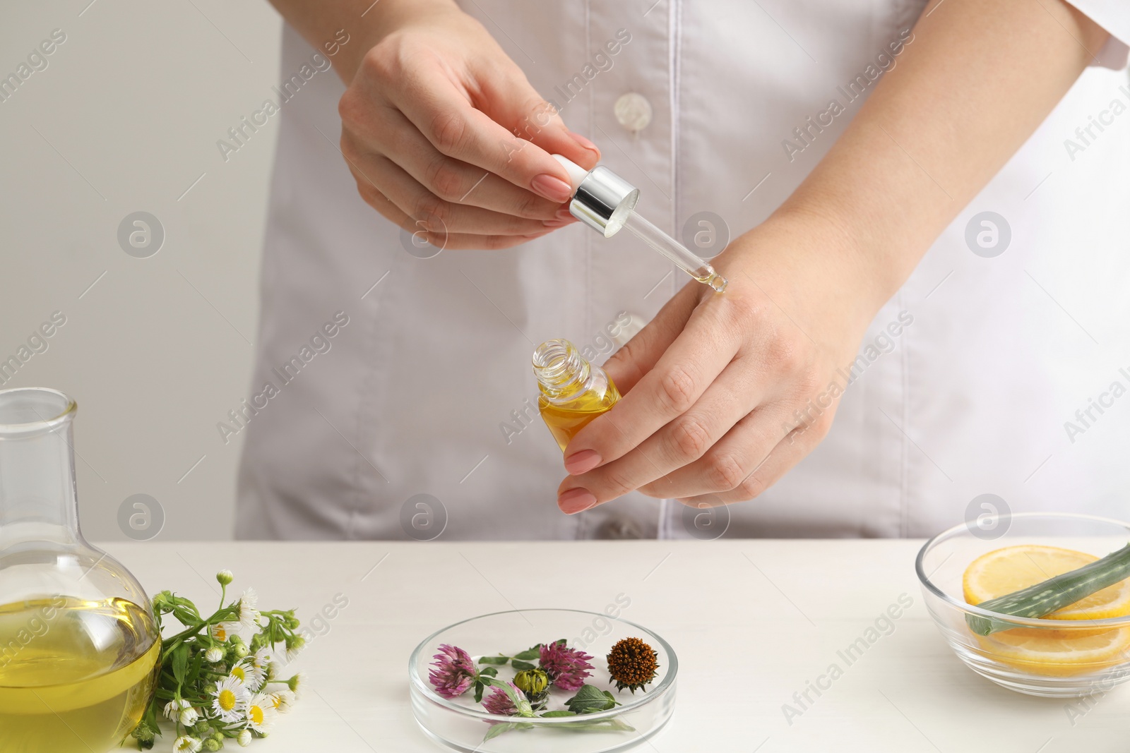 Photo of Scientist testing cosmetic oil at white table, closeup