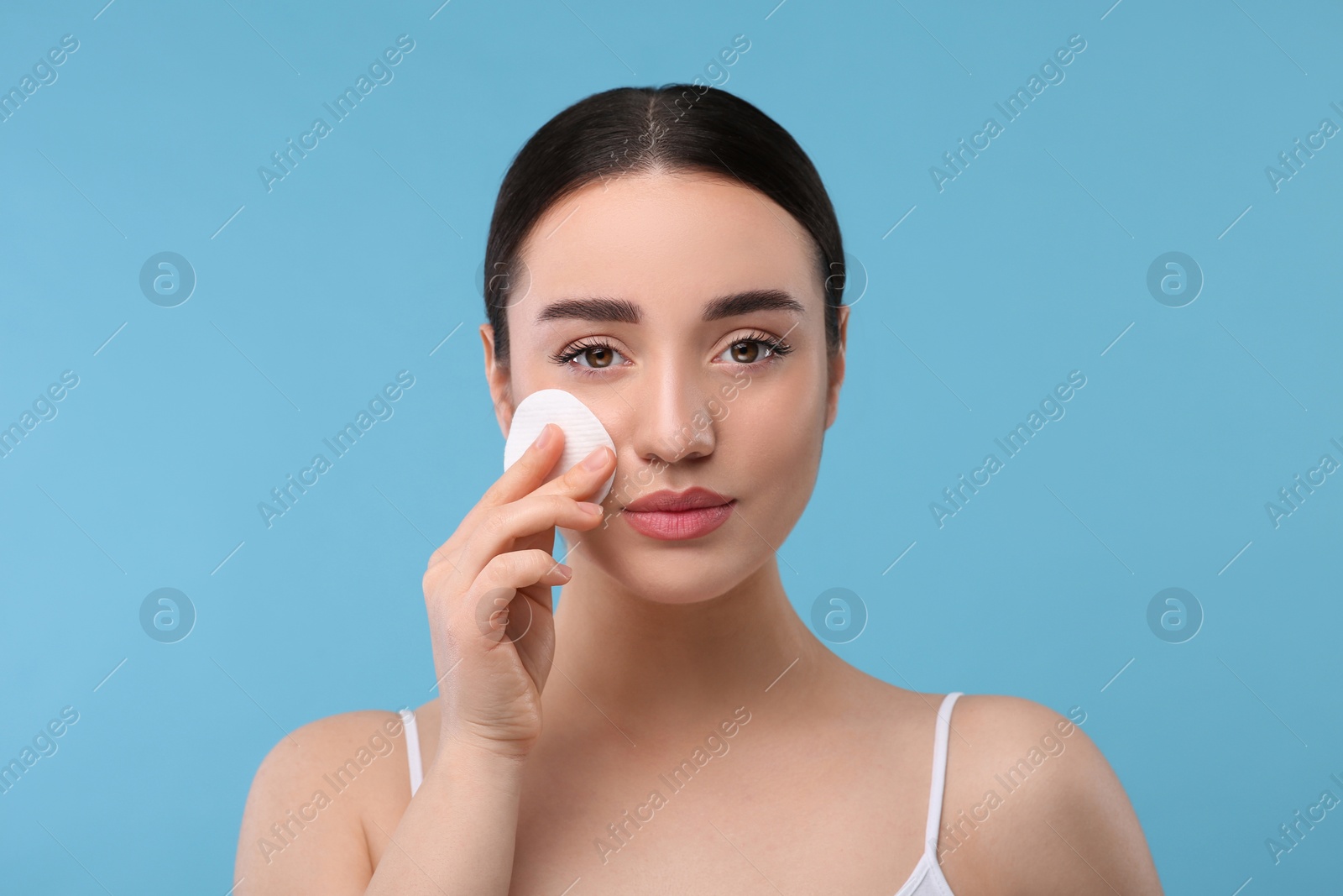 Photo of Beautiful woman removing makeup with cotton pad on light blue background