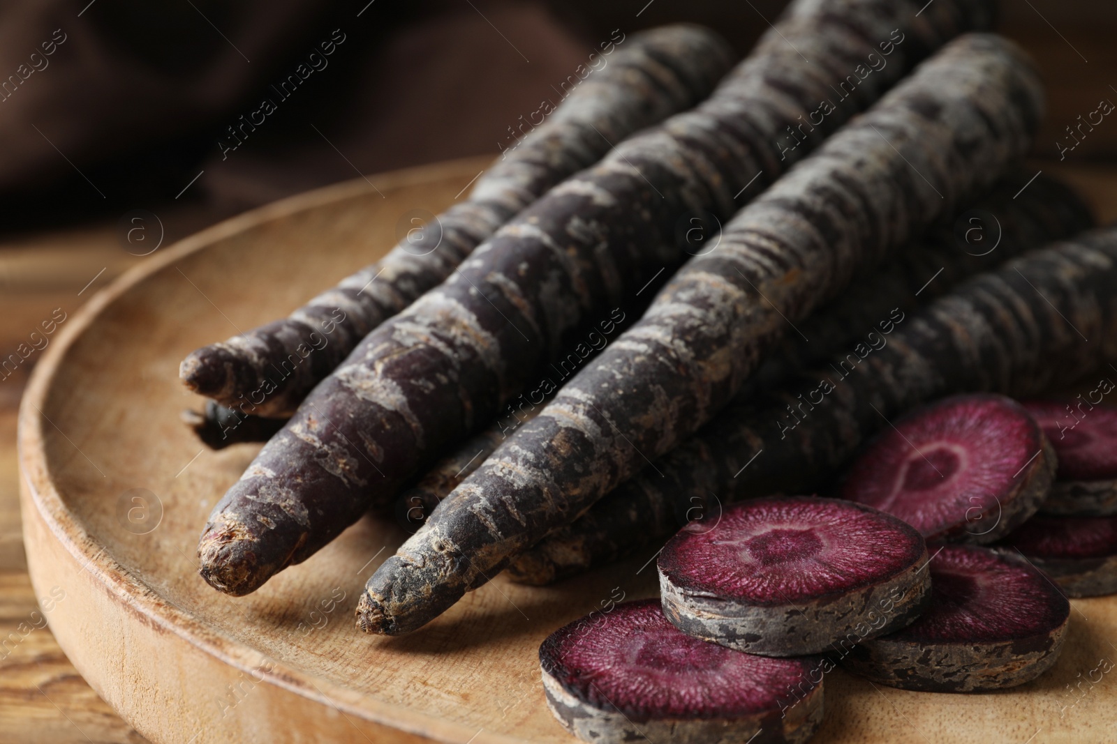 Photo of Raw black carrots on wooden plate, closeup