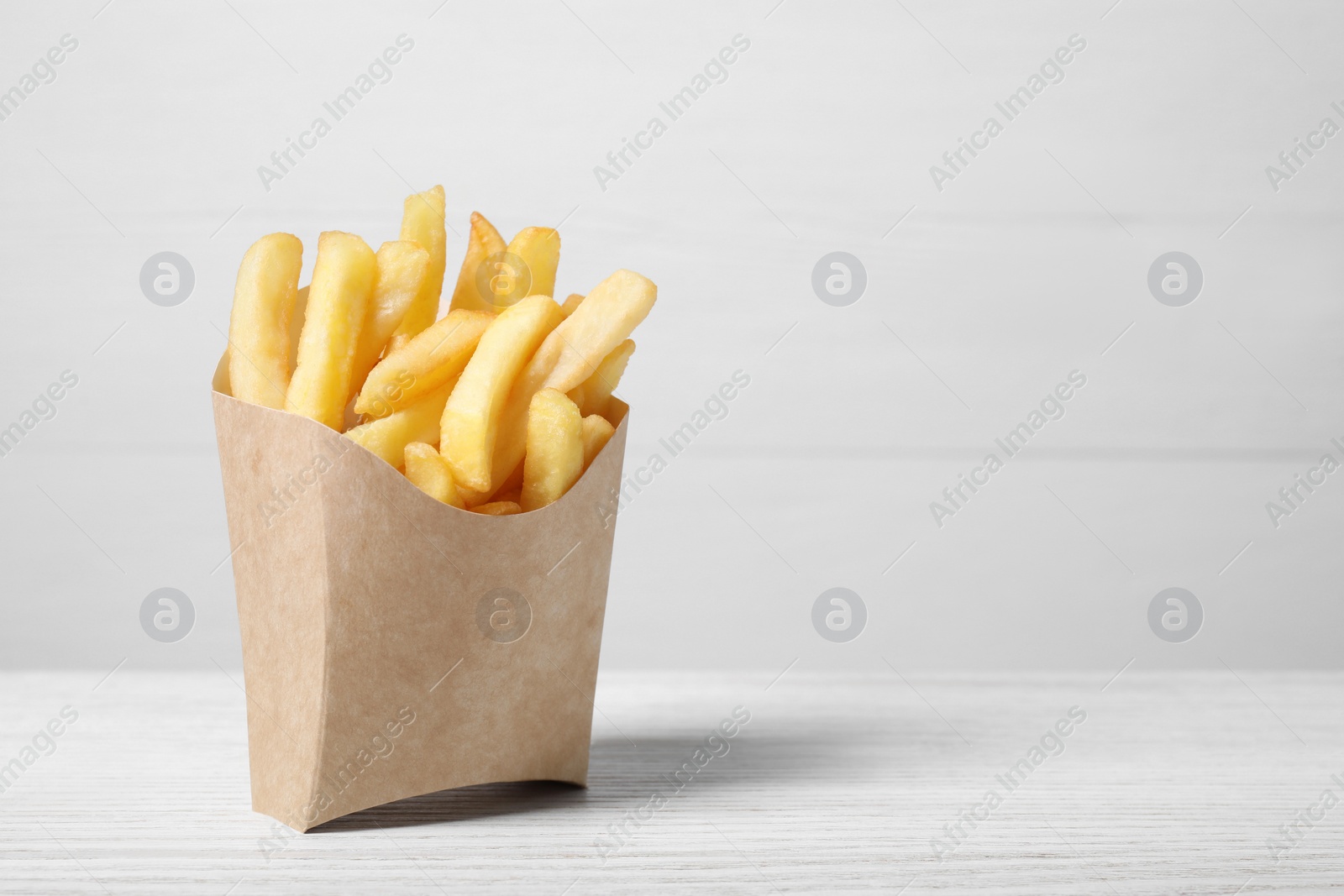 Photo of Delicious french fries in paper box on white wooden table, space for text