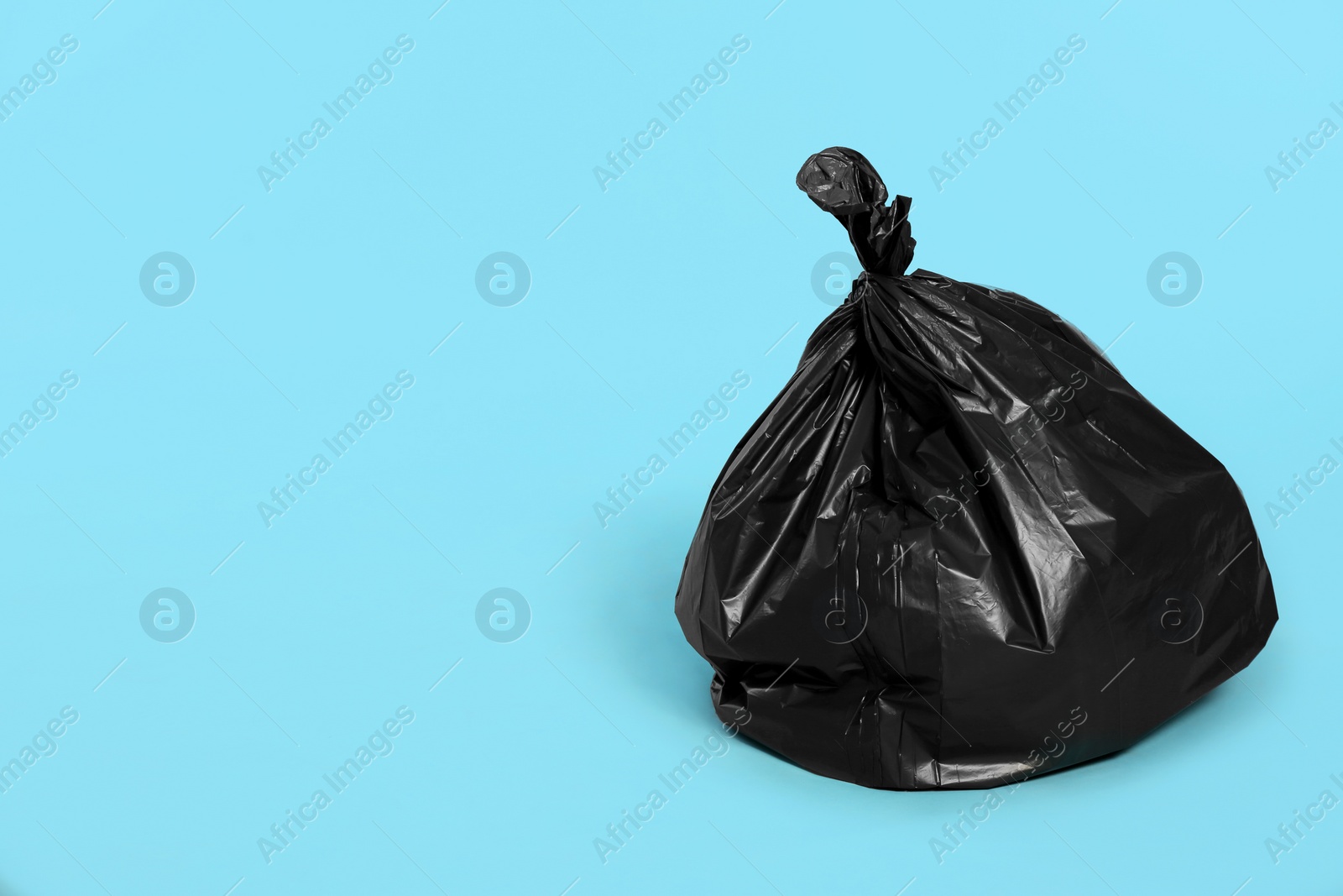 Photo of Trash bag full of garbage on light blue background. Space for text