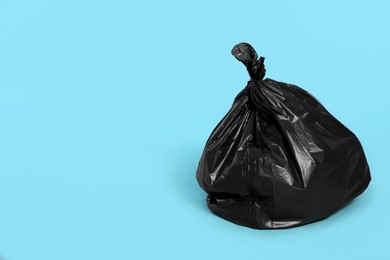 Photo of Trash bag full of garbage on light blue background. Space for text
