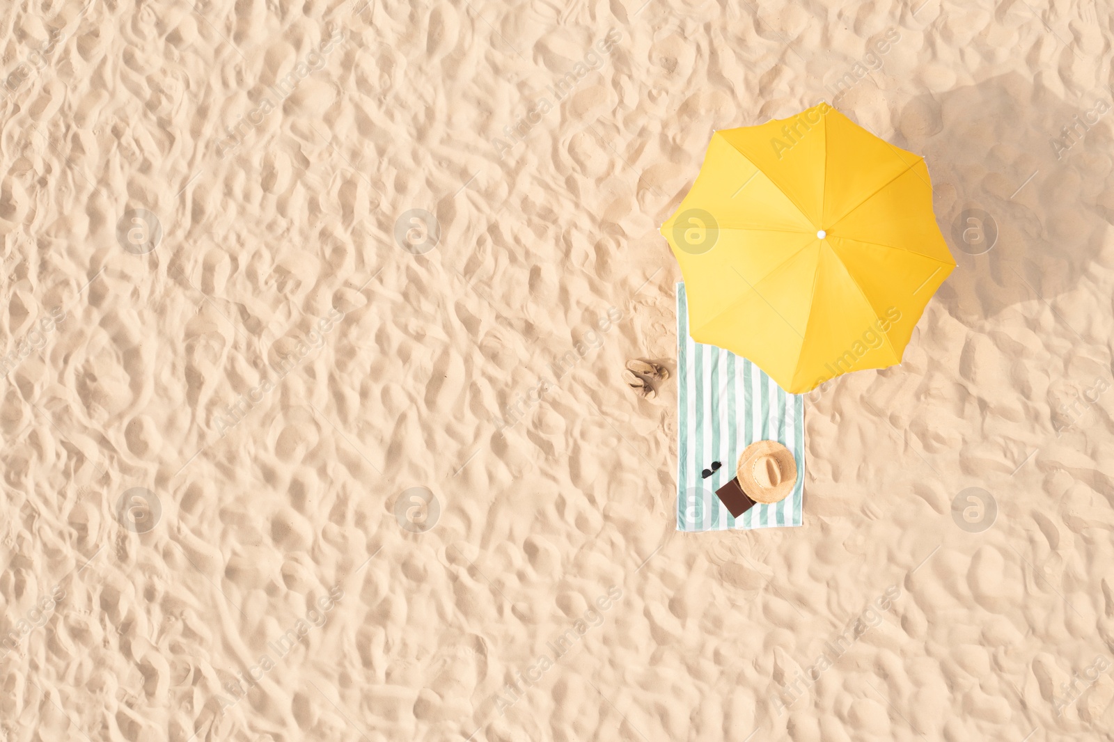 Image of Beach umbrella near towel and other vacationist's stuff on sand, aerial view. Space for text