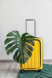 Photo of Bright yellow suitcase with tropical leaf indoors