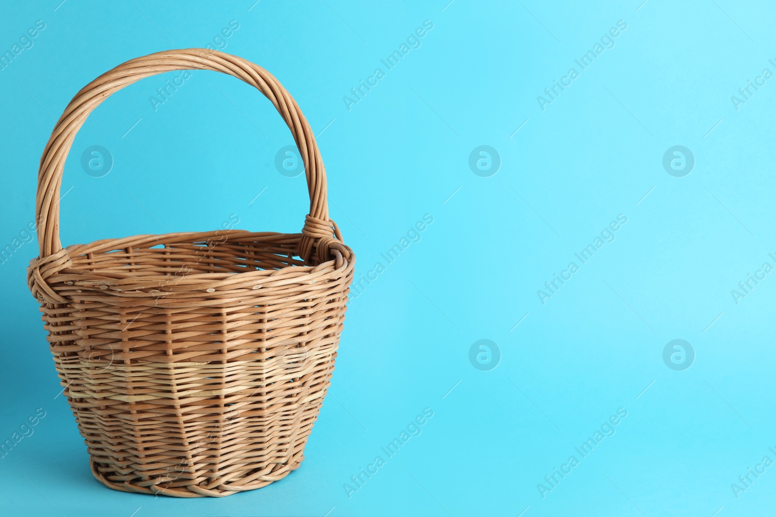 Photo of Empty wicker basket on light blue background, space for text. Easter item