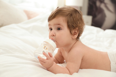 Cute little baby in diaper with bottle on bed