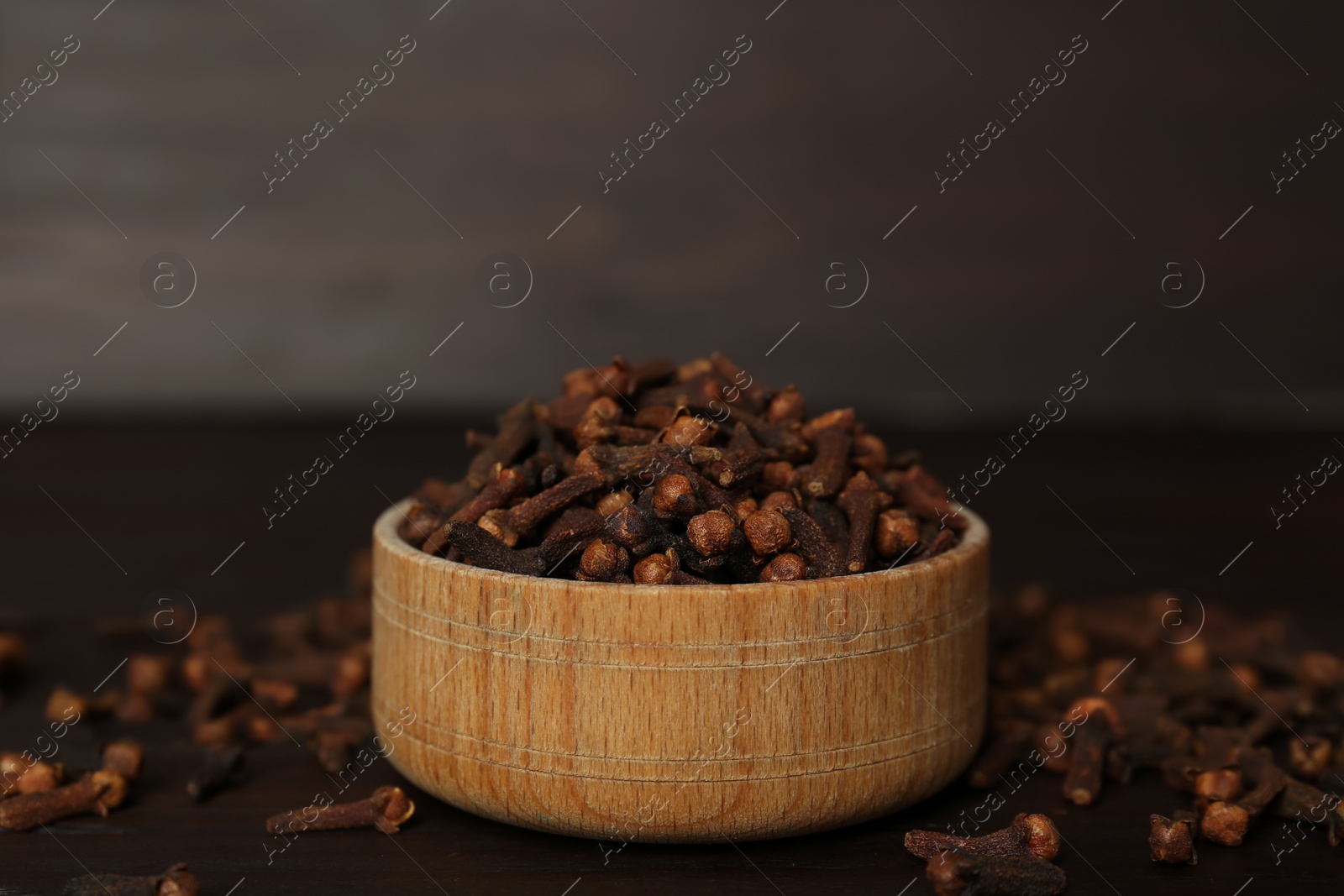 Photo of Bowl and aromatic dry cloves on wooden table