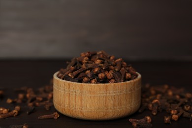 Photo of Bowl and aromatic dry cloves on wooden table