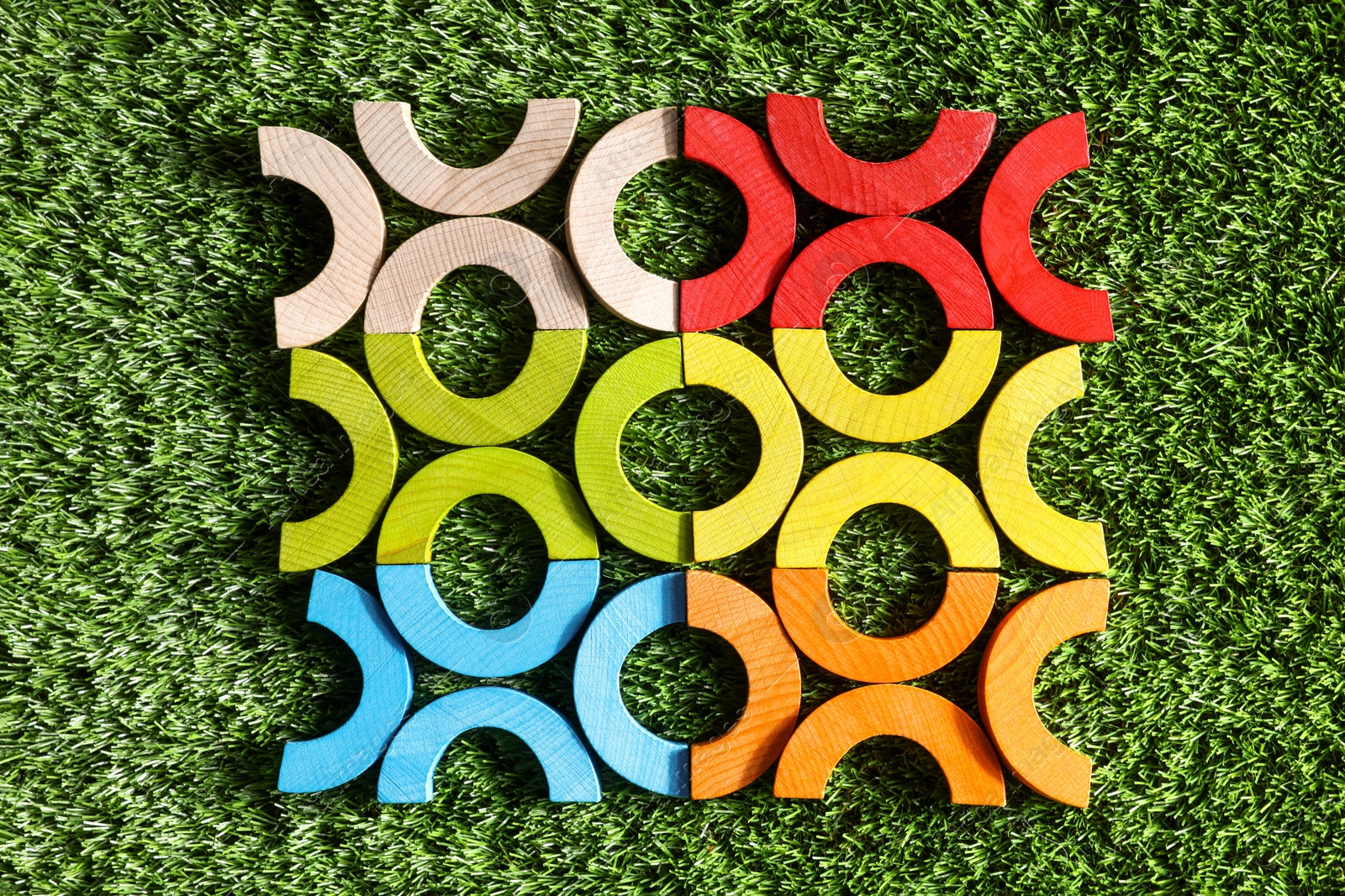 Photo of Colorful wooden pieces of play set on green grass, flat lay. Educational toy for motor skills development