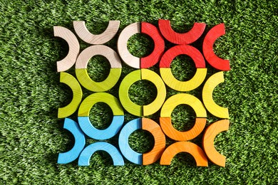 Colorful wooden pieces of play set on green grass, flat lay. Educational toy for motor skills development