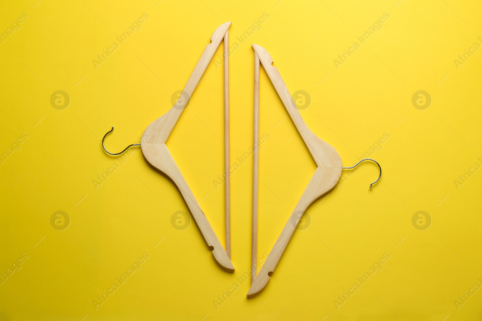 Photo of Wooden hangers on yellow background, top view