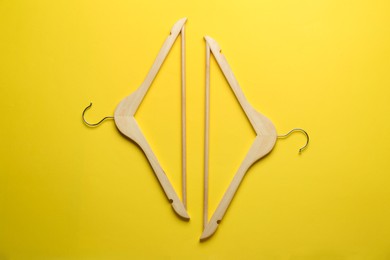 Wooden hangers on yellow background, top view