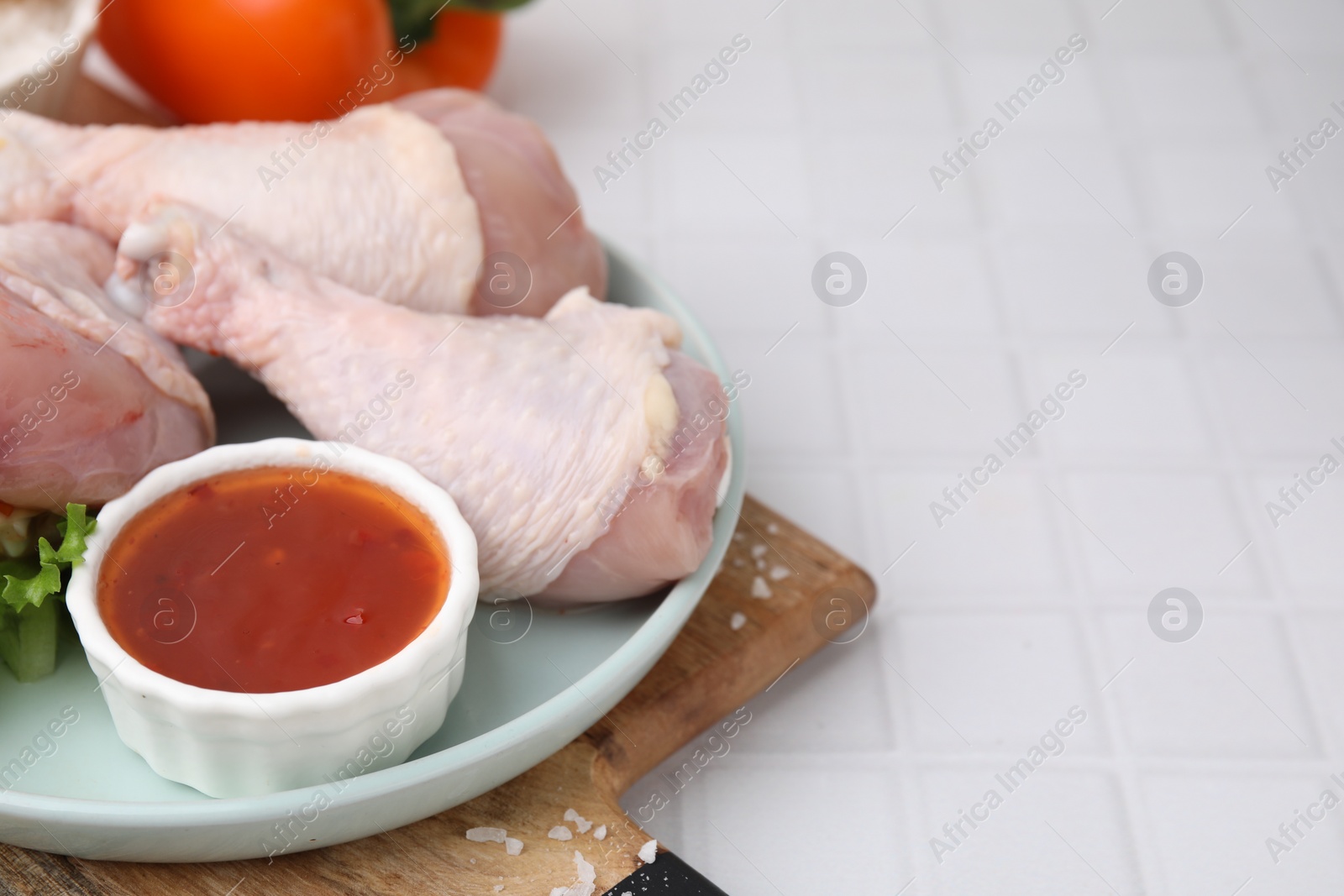 Photo of Fresh marinade and raw chicken drumsticks on white tiled table. Space for text