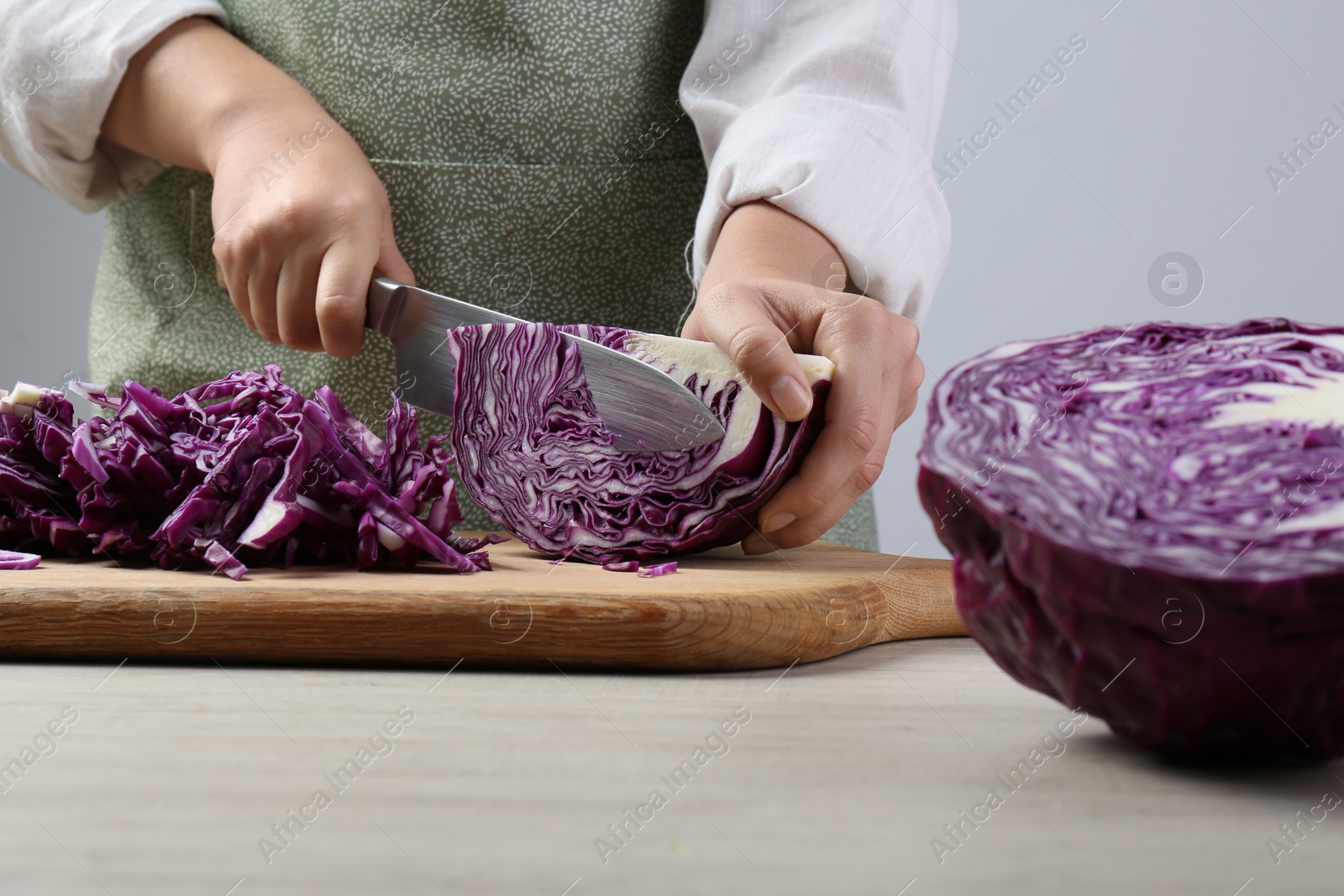 Photo of Woman cutting fresh radicchio cabbage on board at wooden table, closeup