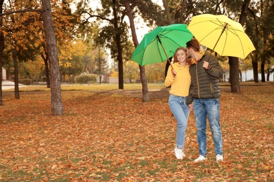 Photo of Happy couple with umbrellas walking in park. Space for text