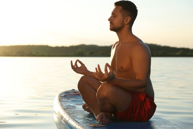 Man meditating on SUP board on river at sunset