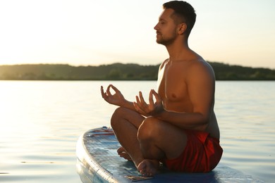 Photo of Man meditating on SUP board on river at sunset