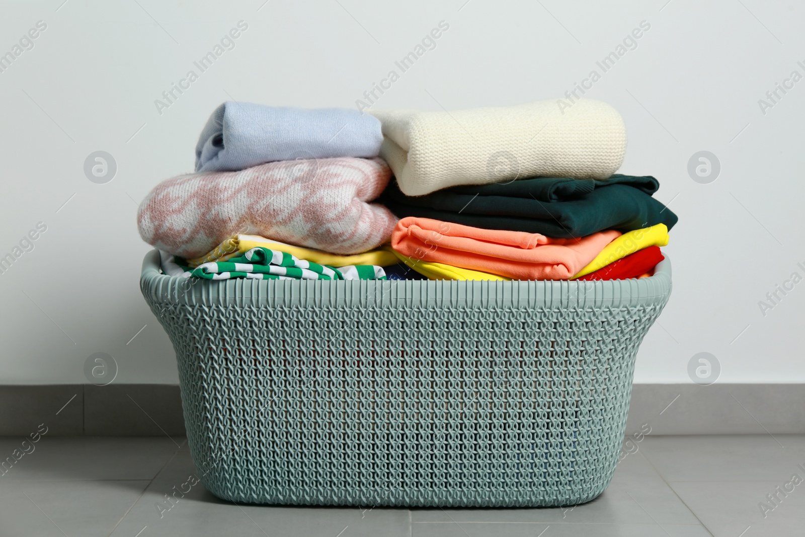 Photo of Plastic laundry basket with clean clothes on floor indoors