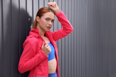 Beautiful woman in gym clothes posing near dark grey fence on street, space for text