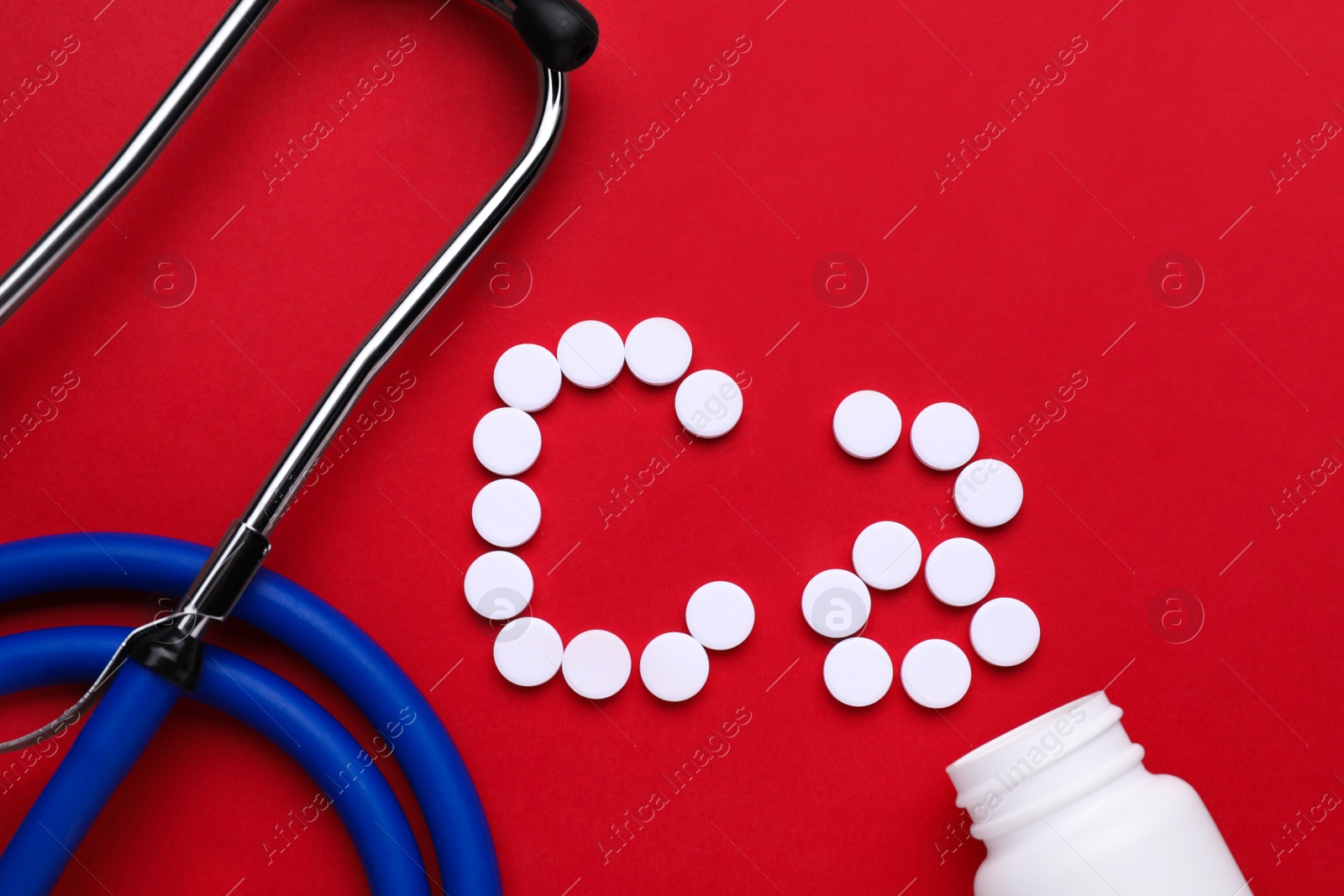 Photo of Stethoscope and calcium symbol made of white pills on red background, flat lay