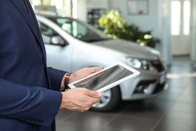 Photo of Young car salesman with tablet in dealership, closeup