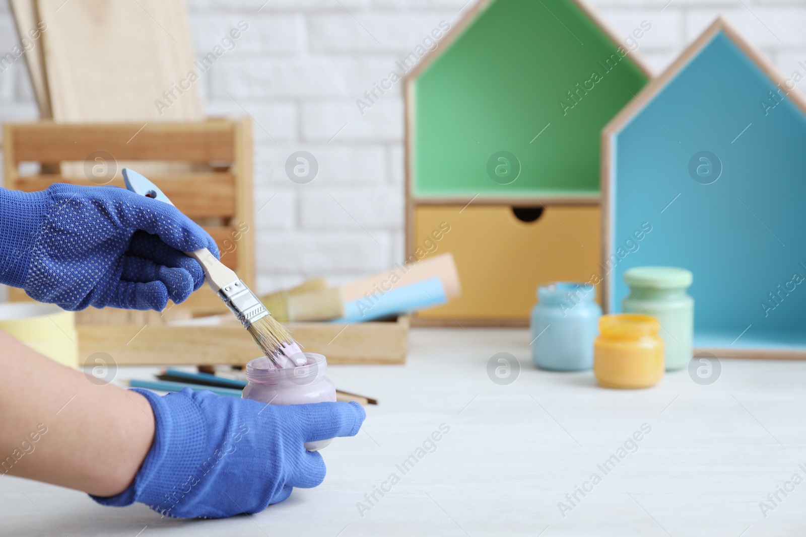 Photo of Decorator holding jar of violet paint and brush at white table, closeup. Space for text