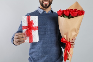 Happy man with red tulip bouquet and gift box on light grey background, closeup. 8th of March celebration