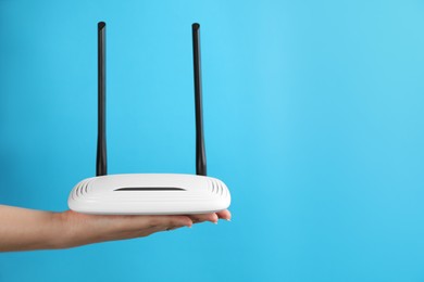 Photo of Woman holding modern Wi-Fi router on light blue background, closeup. Space for text