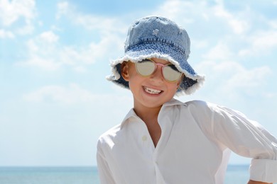 Photo of Little girl wearing sunglasses and hat at beach on sunny day. Space for text