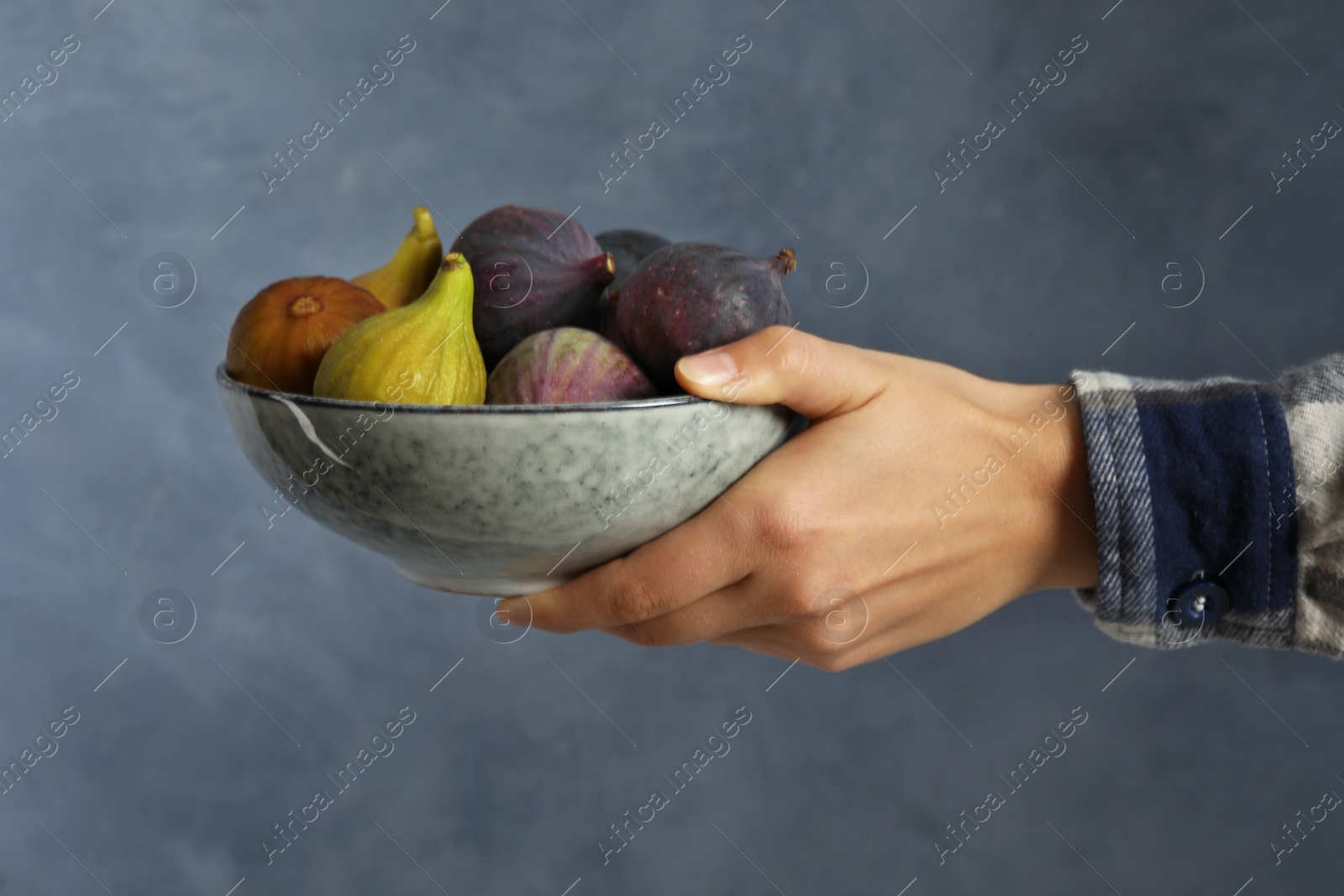 Photo of Woman holding bowl with tasty raw figs on light blue background, closeup