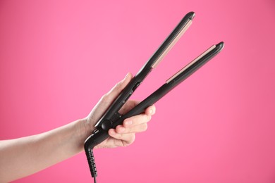 Photo of Woman holding corrugated hair iron on pink background, closeup