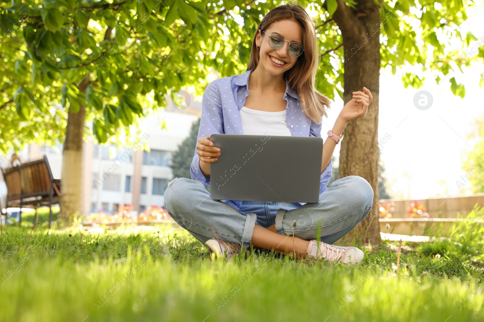 Image of Happy young woman with laptop sitting on green grass in park