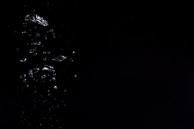 Air bubbles in water on black background, space for text