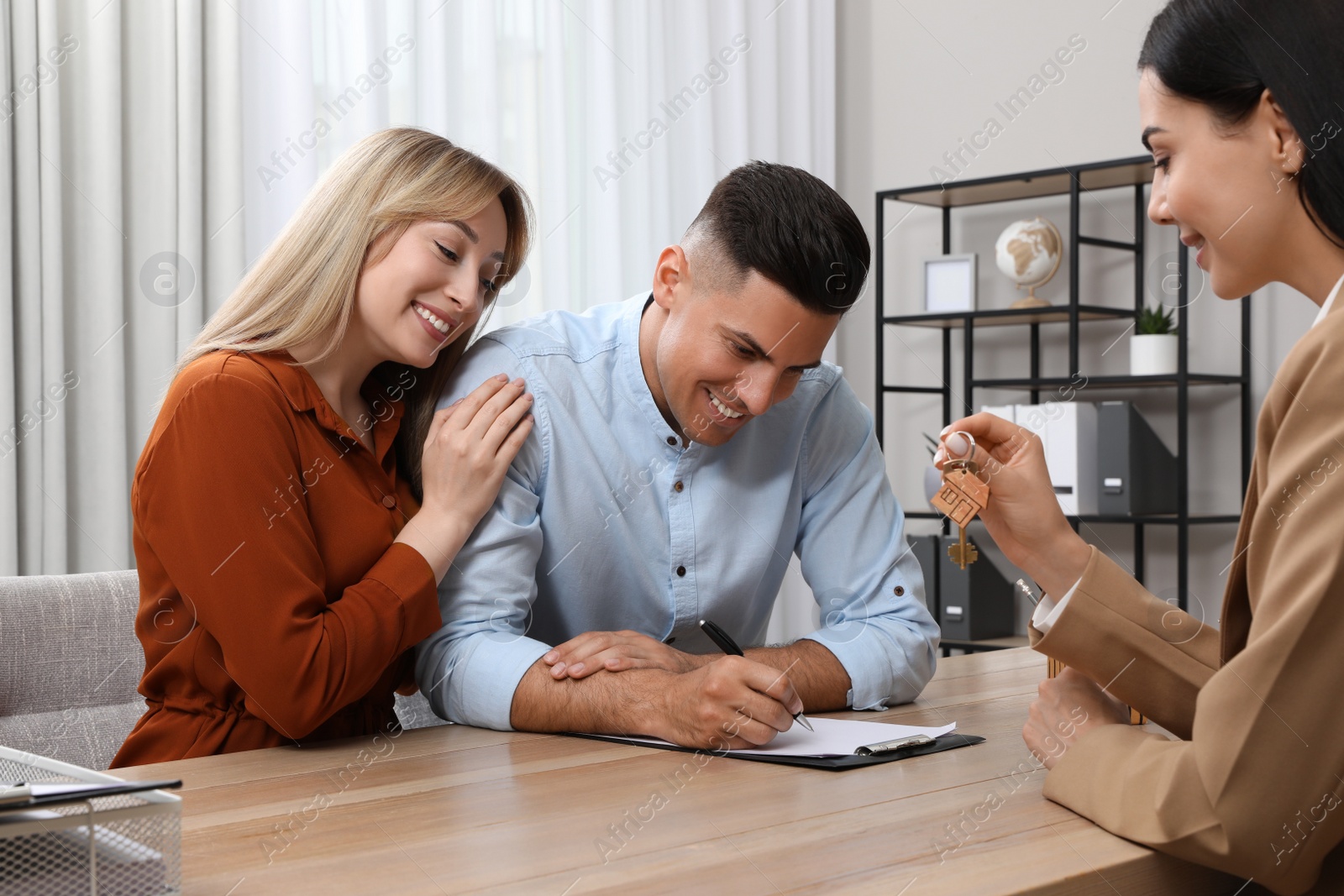 Photo of Real estate agent giving house key to couple at table in office