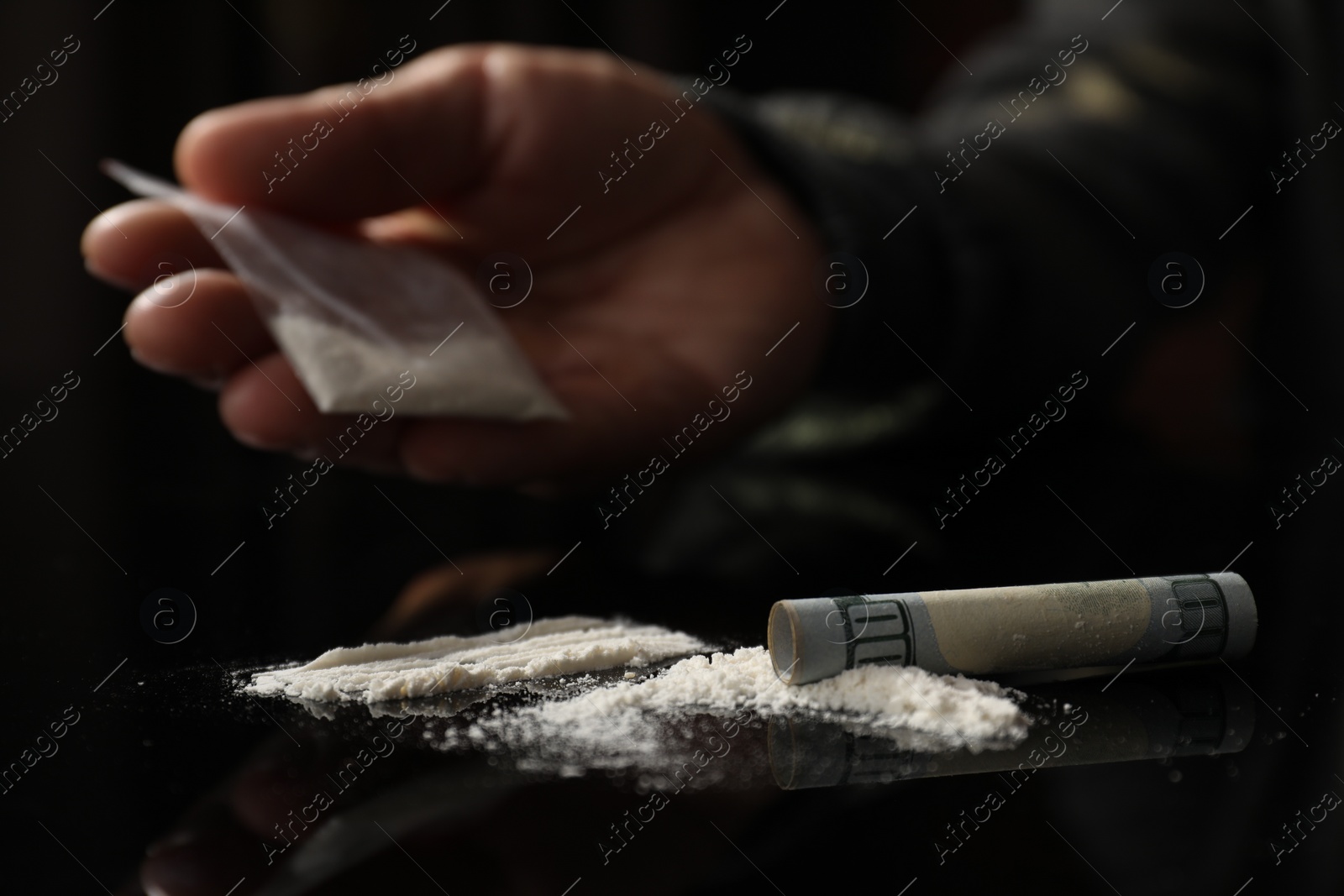 Photo of Drug addiction. Man with cocaine and rolled dollar banknote at black table, selective focus