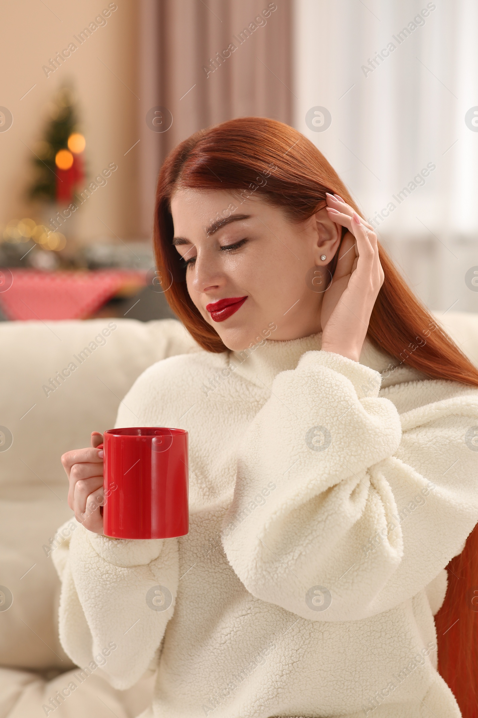 Photo of Beautiful young woman with cup of tea on sofa at home. Celebrating Christmas
