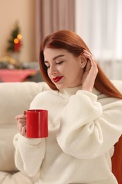 Photo of Beautiful young woman with cup of tea on sofa at home. Celebrating Christmas
